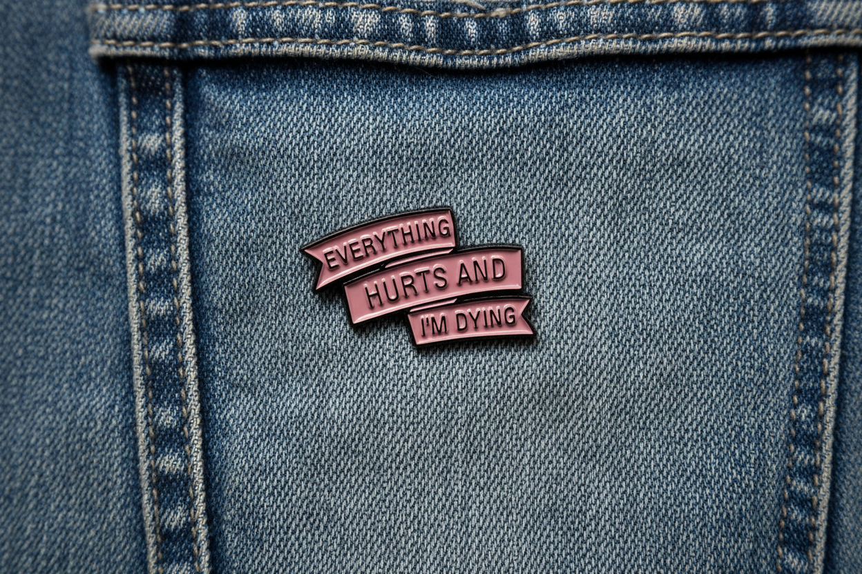 Metallic pink enamel pin with text on a denim background