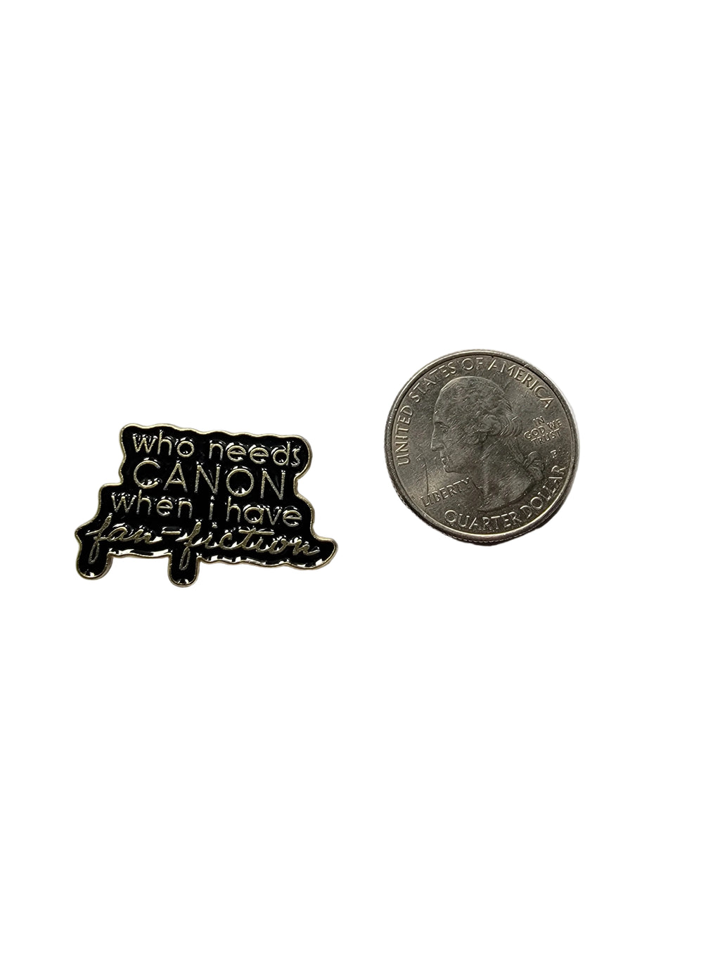 a black enamel pin with gold text next to a quarter for scale on a white background