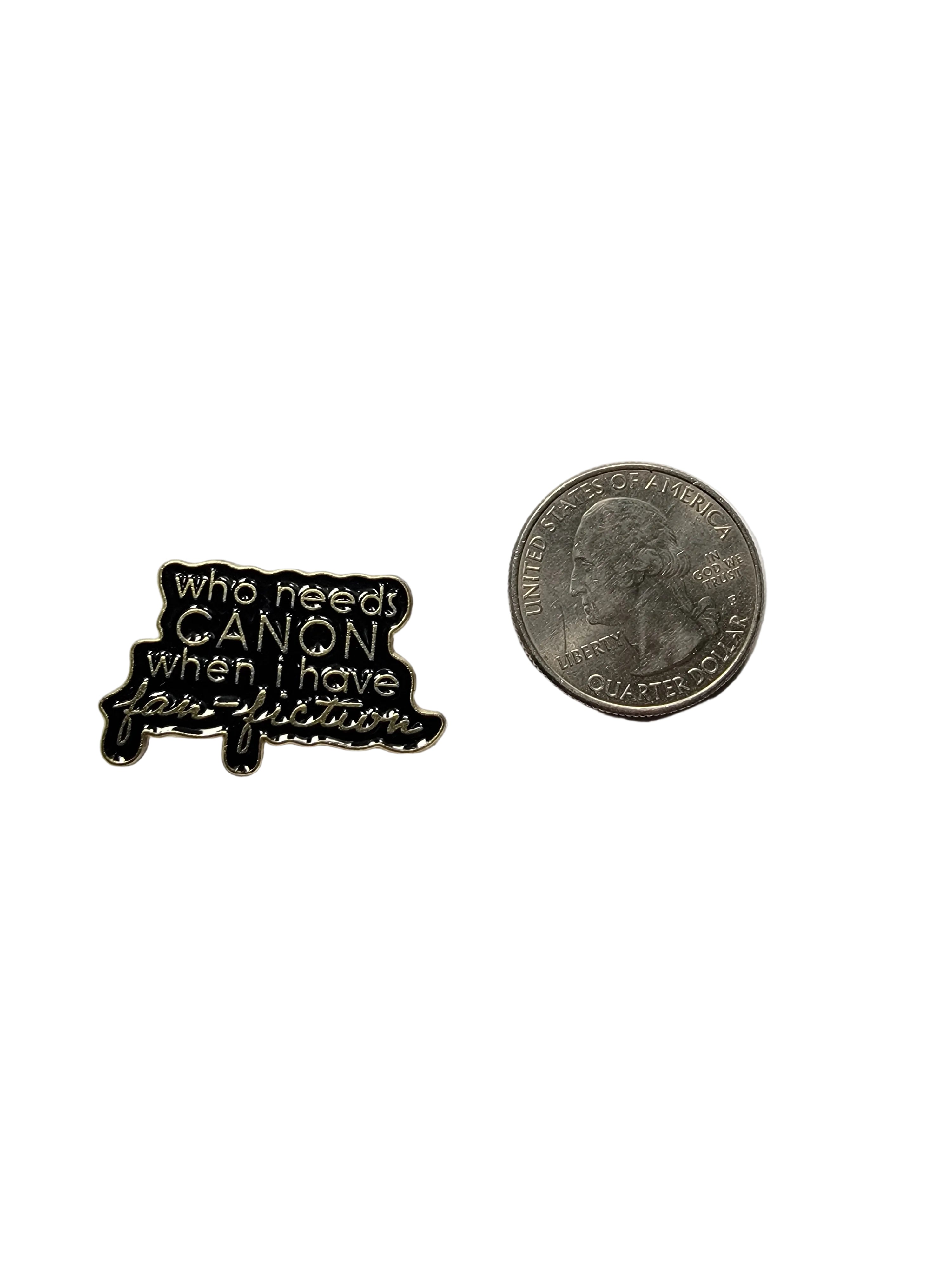 a black enamel pin with gold text next to a quarter for scale on a white background
