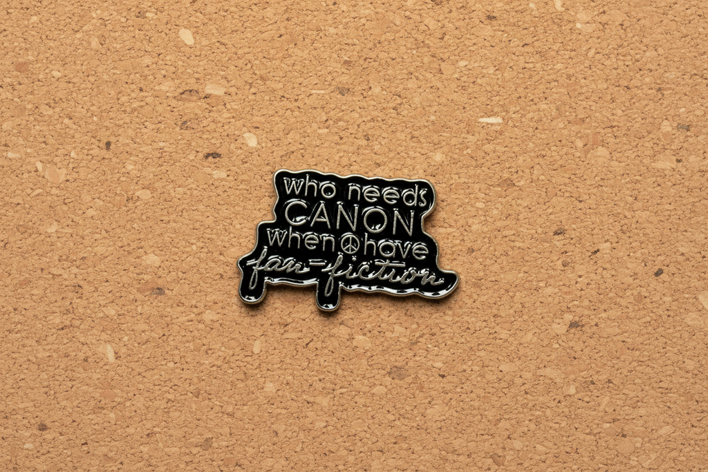 a black enamel pin with gold text on a cork background