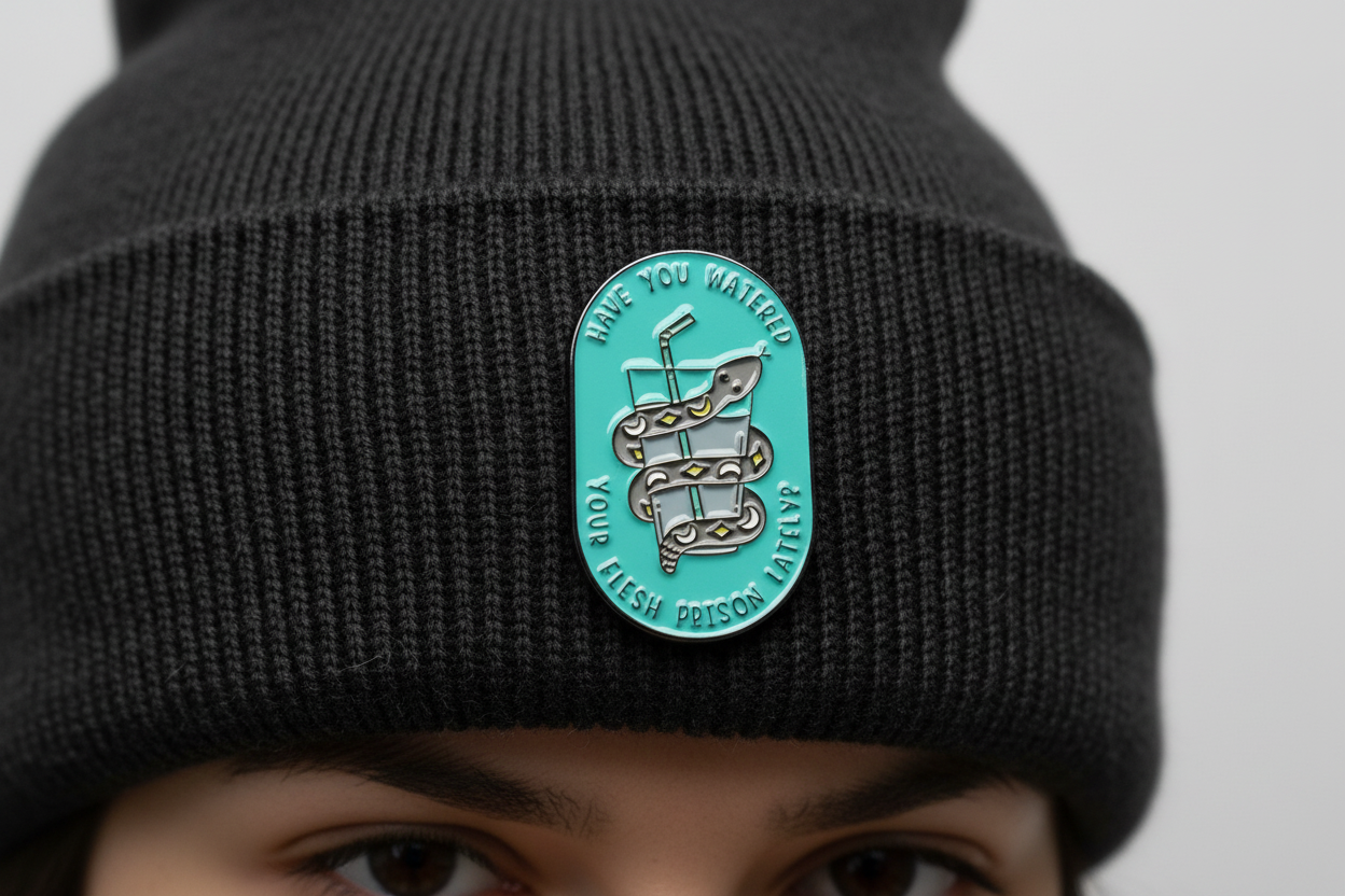 a teal pin with a snake and water on a black beanie background