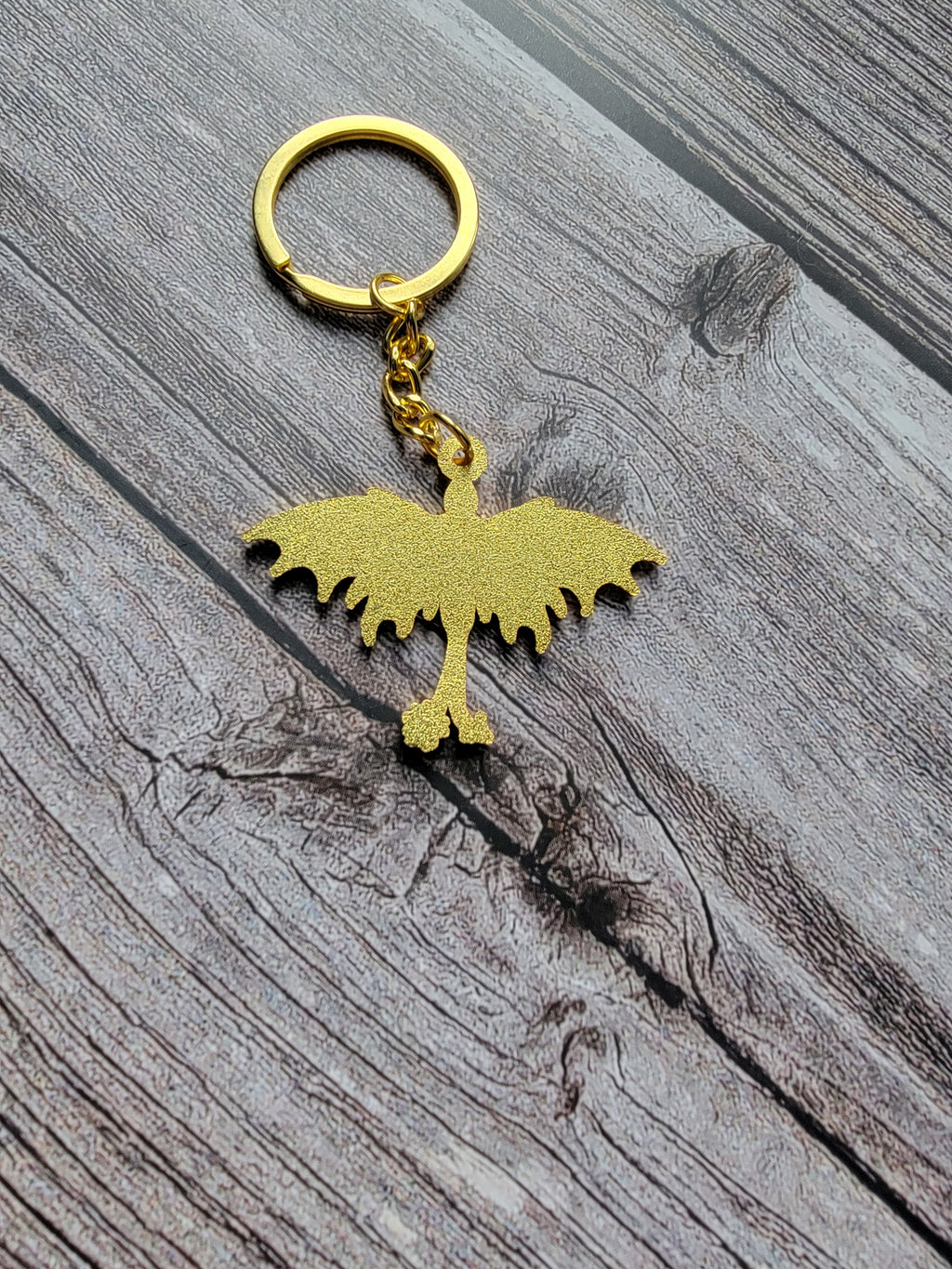 Gold bird-shaped keychain on a wooden surface