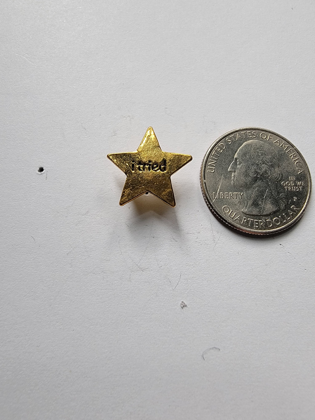 Small gold star pin next to a quarter on a white background
