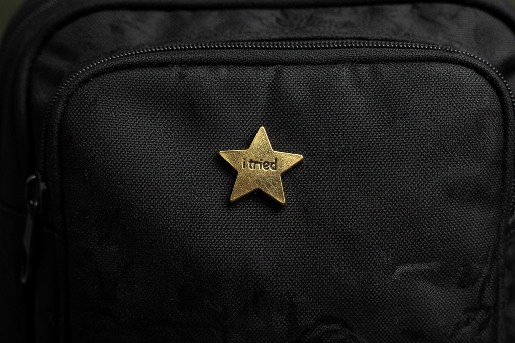 Gold star-shaped object with 'i tried ' engraved on a black fabric background