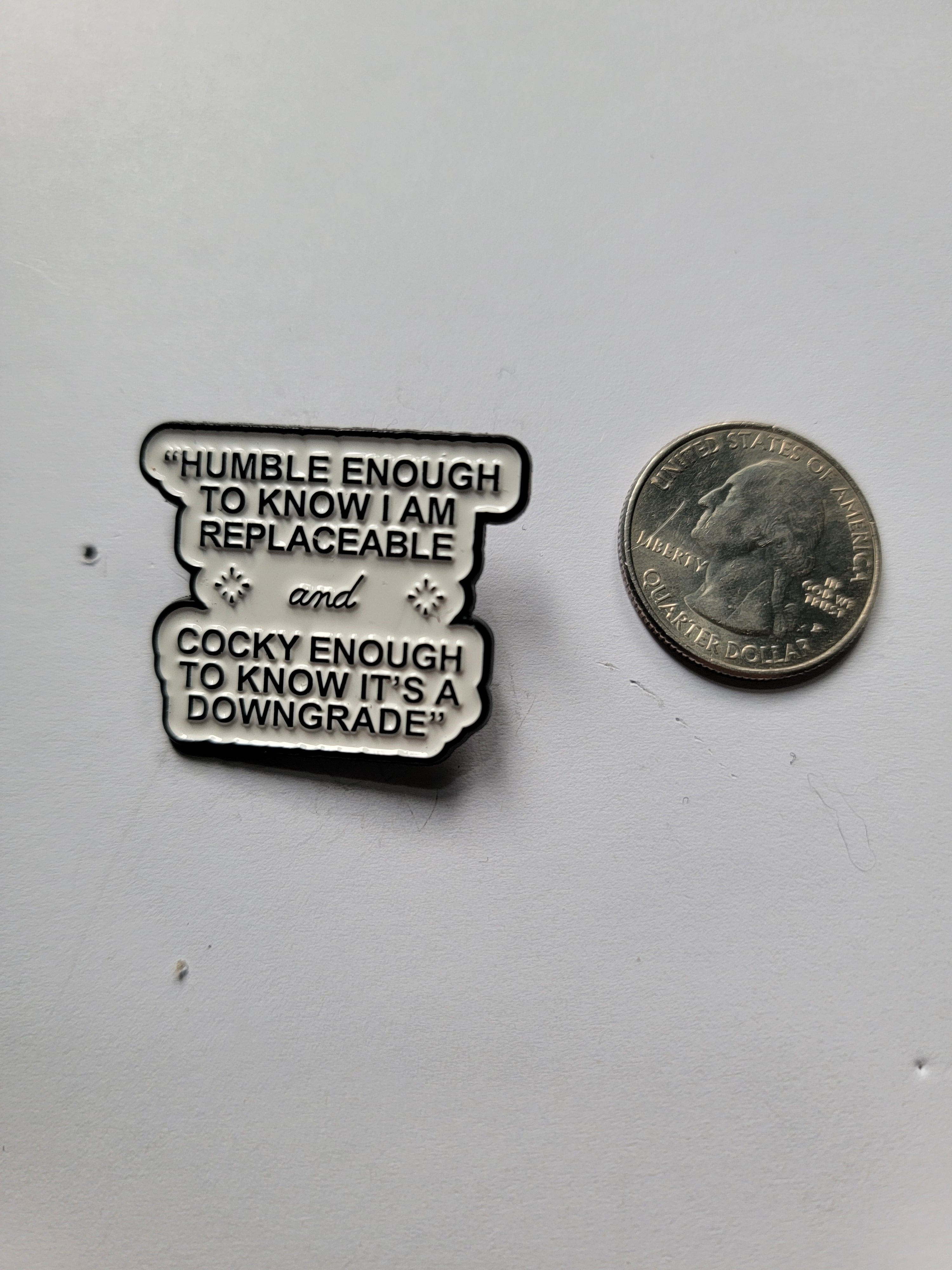 white enamel pin with black text next to a quarter on a white background