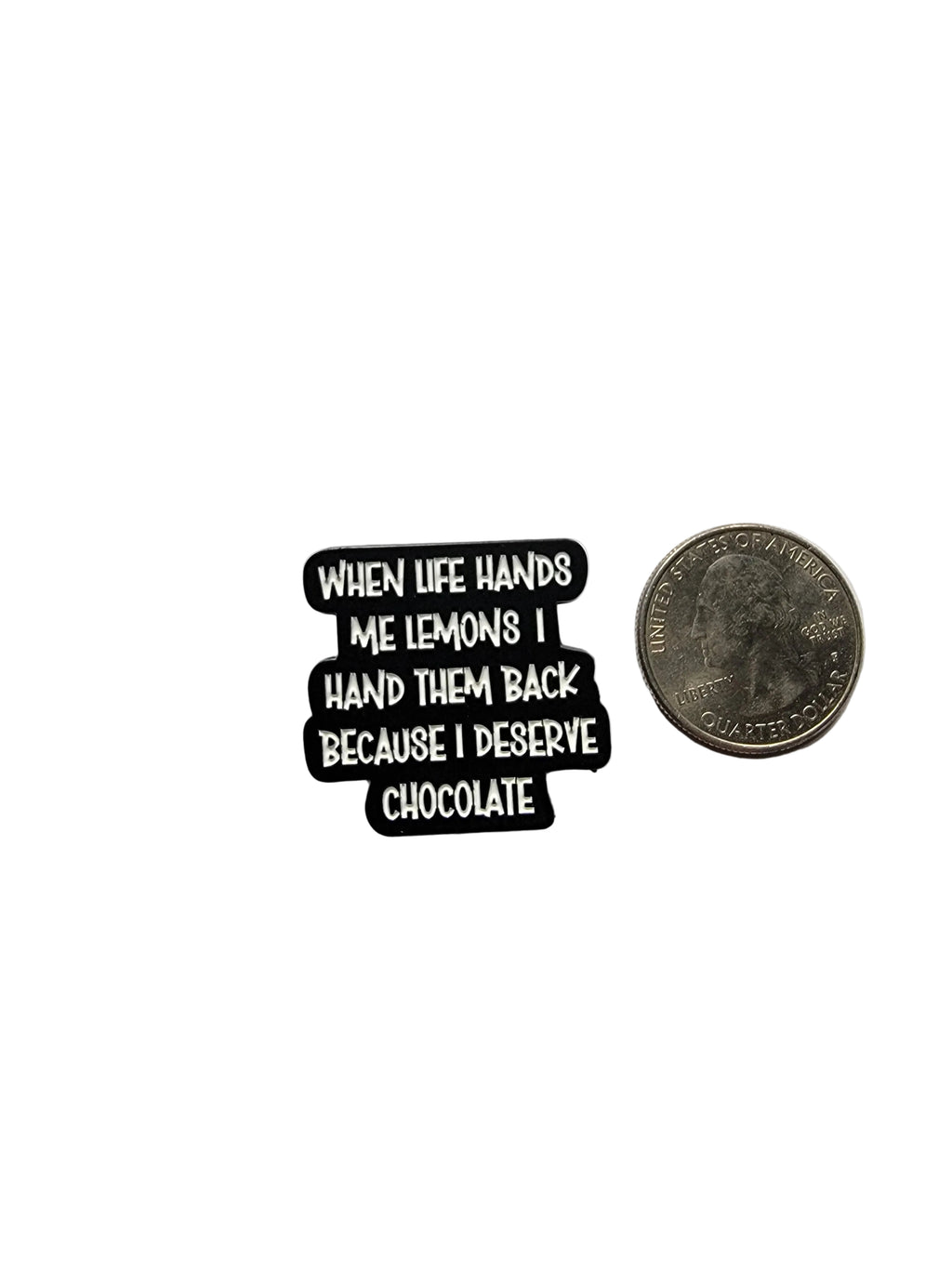 a black enamel pin with with text and a funny quote next to a quarter for scale on a white background