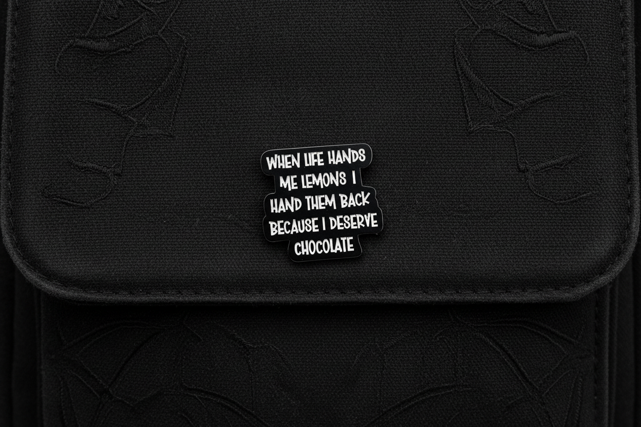a black pin with white text with a funny quote on a black bookbag background