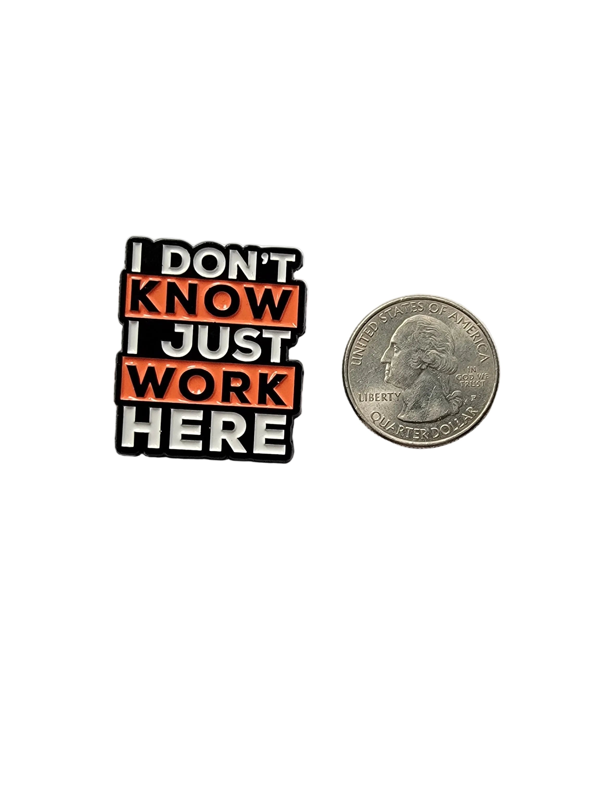 Small metal badge with text 'I DON'T KNOW JUST WORK HERE' next to a quarter on a gray background