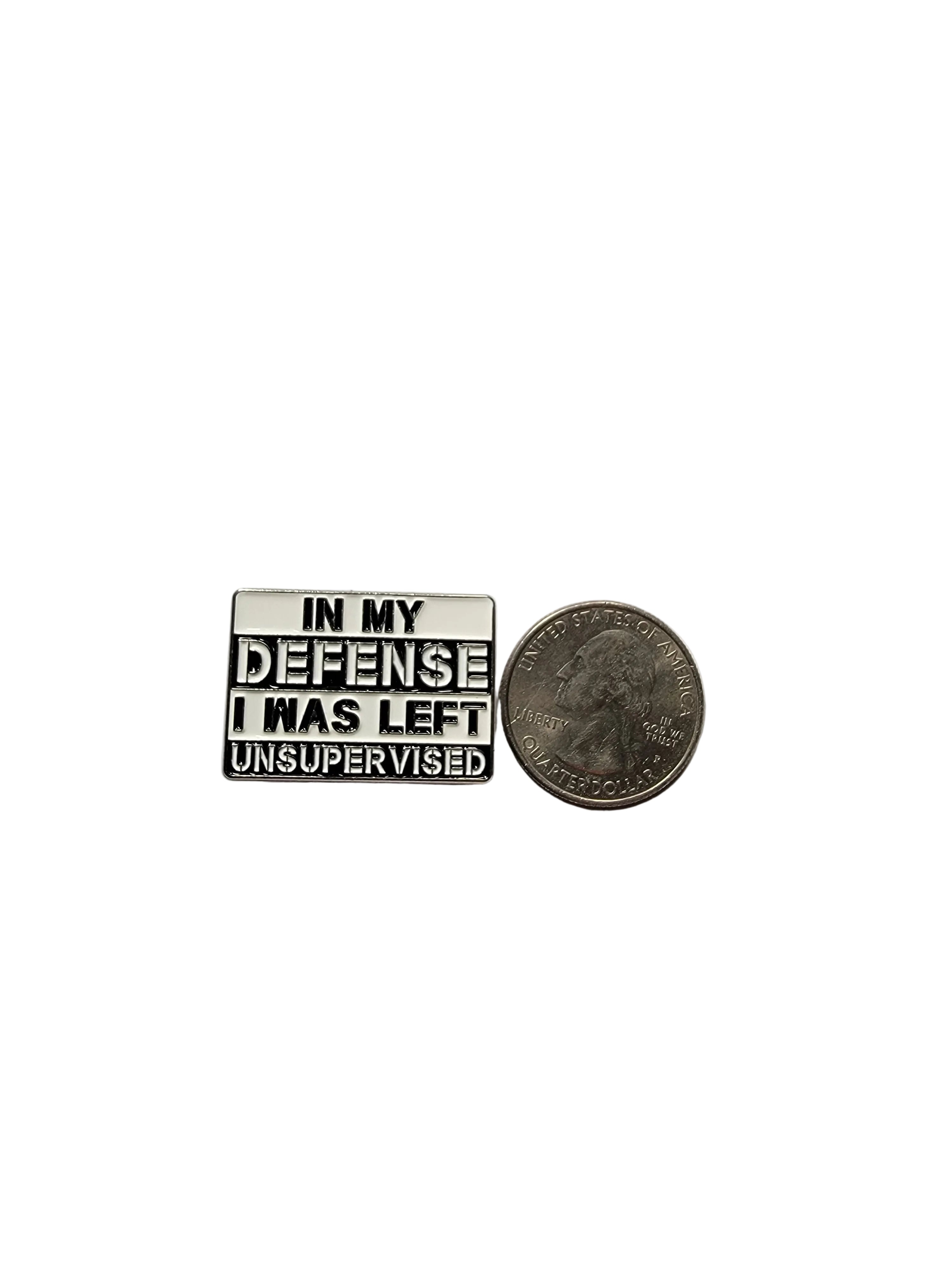 Small metal badge with text 'In my defense I have left unsupervised' next to a quarter on a gray background