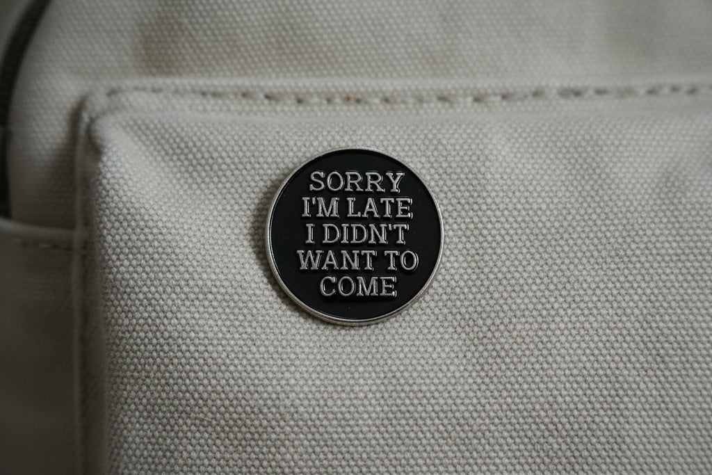 Round black metal badge with silver text on a light gray backpack.