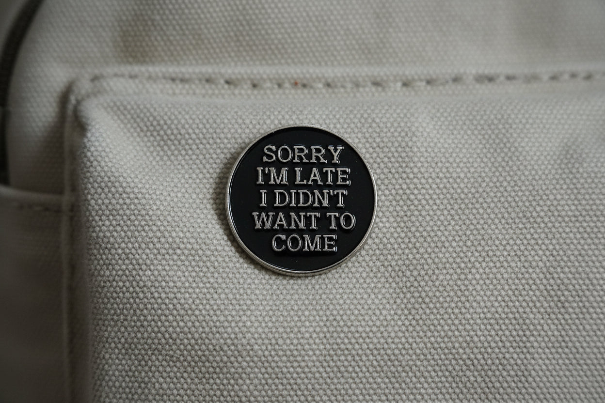 Round black metal badge with silver text on a light gray backpack.