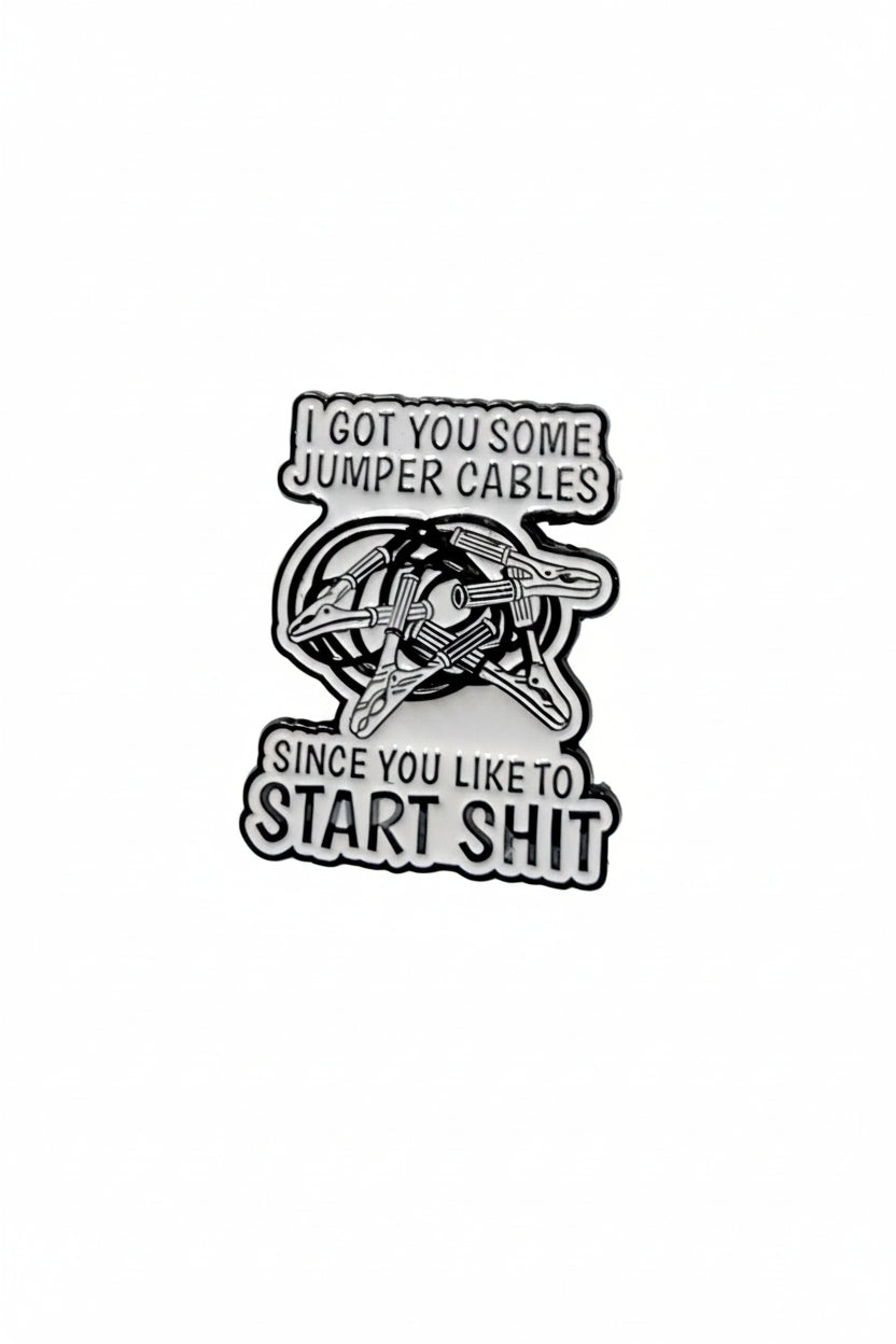 white enamel pin with black text and jumper cables on it on a white background