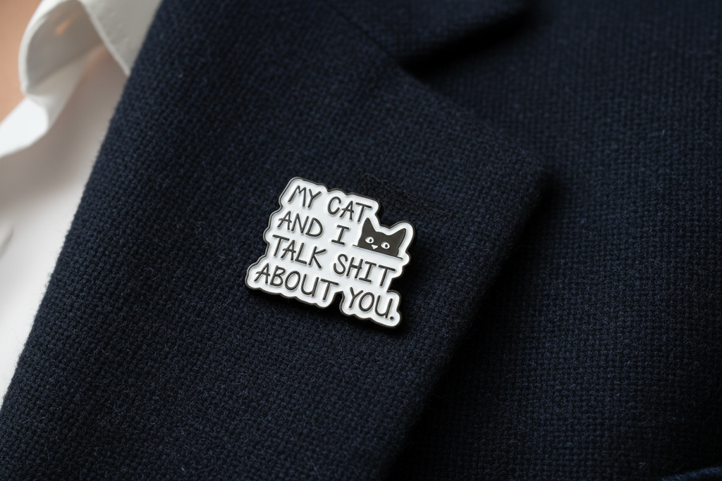 Metallic badge with text 'My cat and I talk shit about you' on a navy lapel background