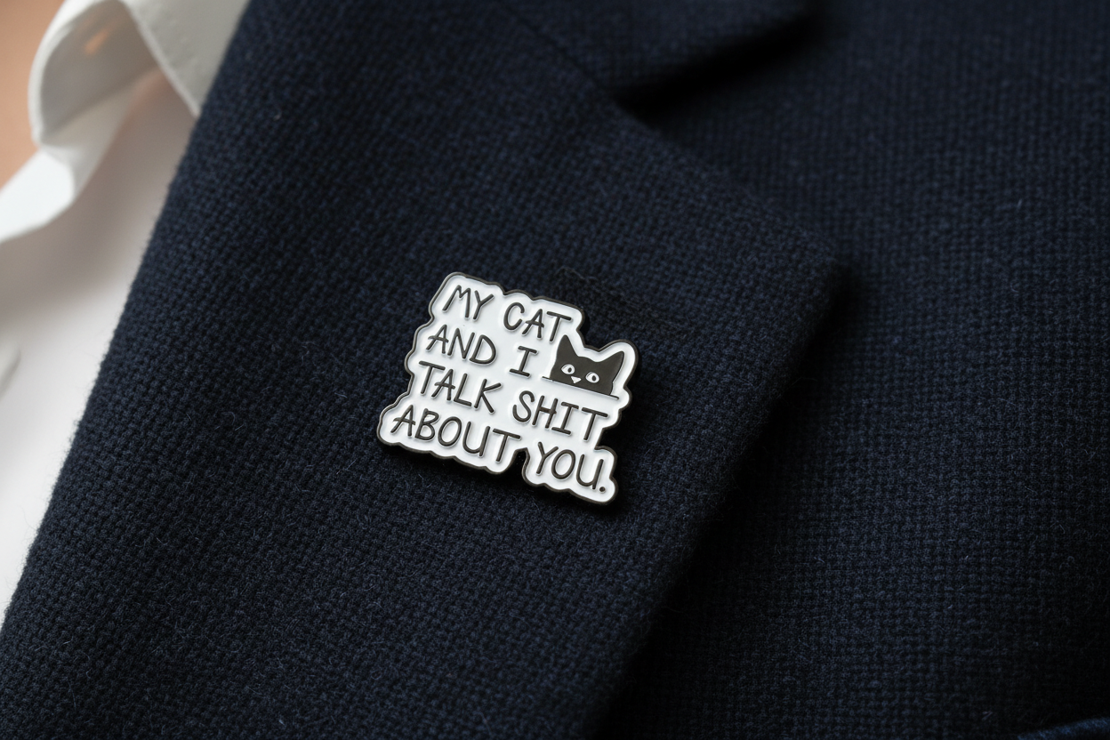 Metallic badge with text 'My cat and I talk shit about you' on a navy lapel background