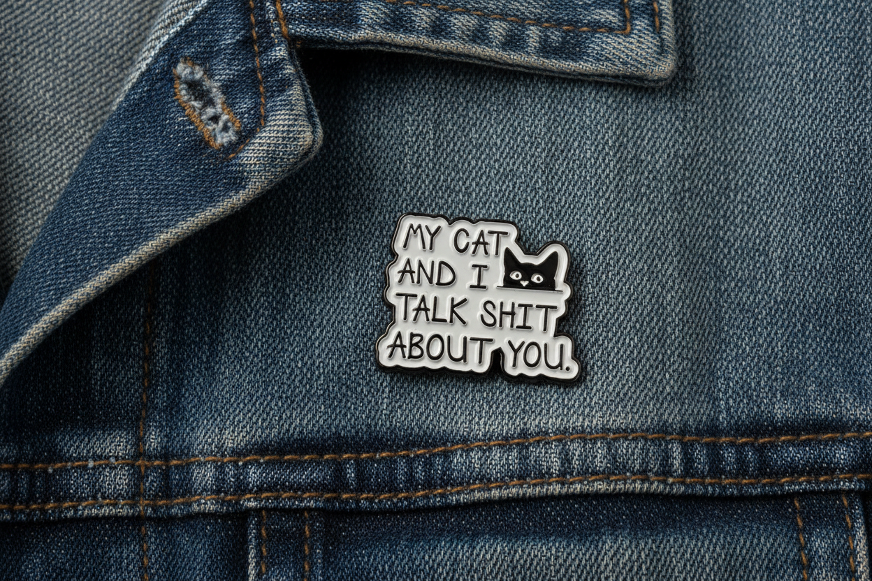 Metallic badge with text 'My cat and I talk shit about you' on a denim jacket background