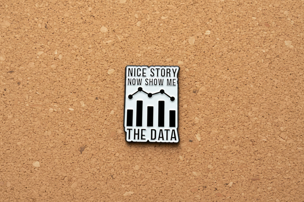 Metallic badge with text 'Nice story, now show me the data' on a cork background