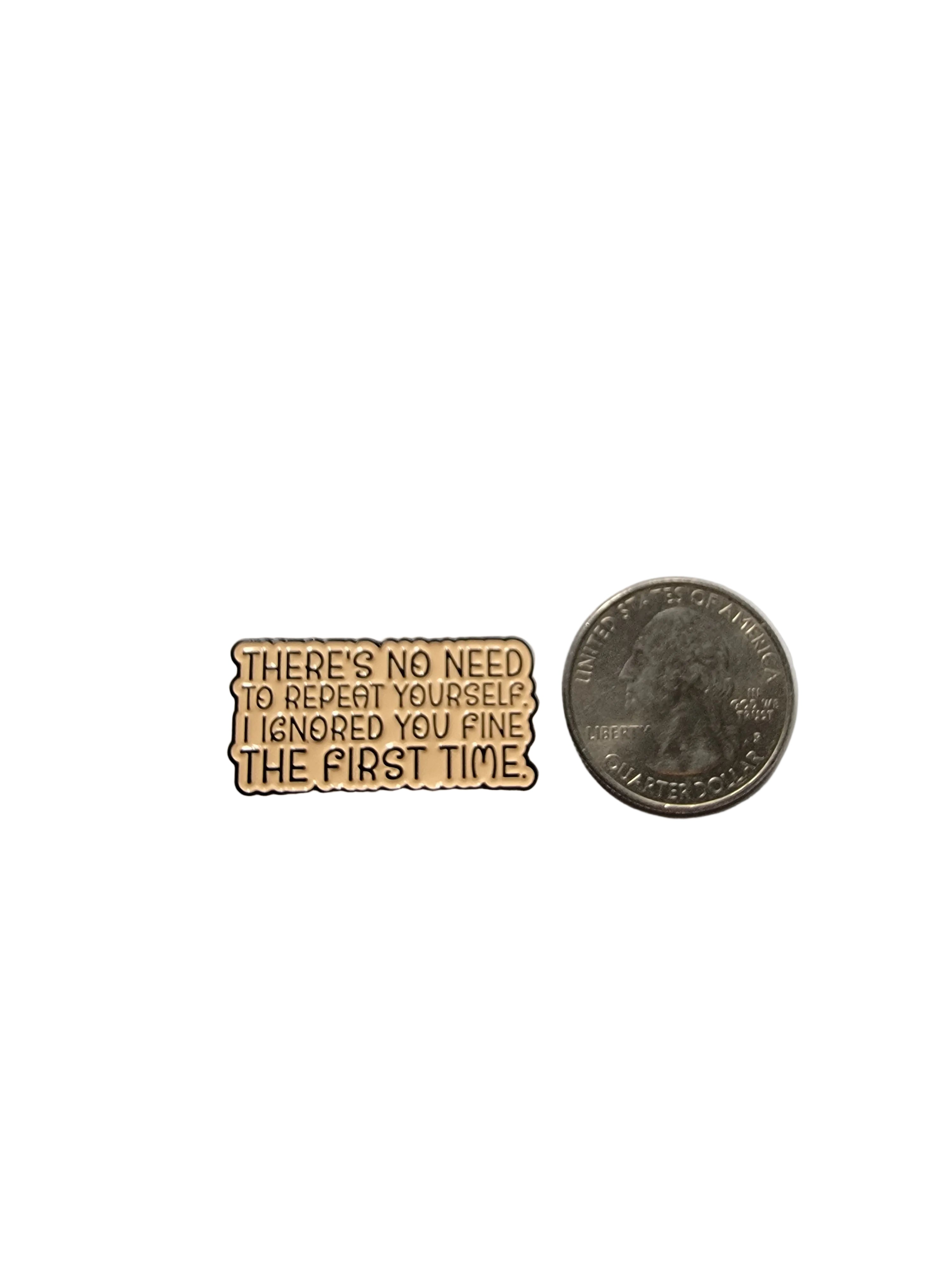 a beige pin with black text next to a quarter for scale with a white background
