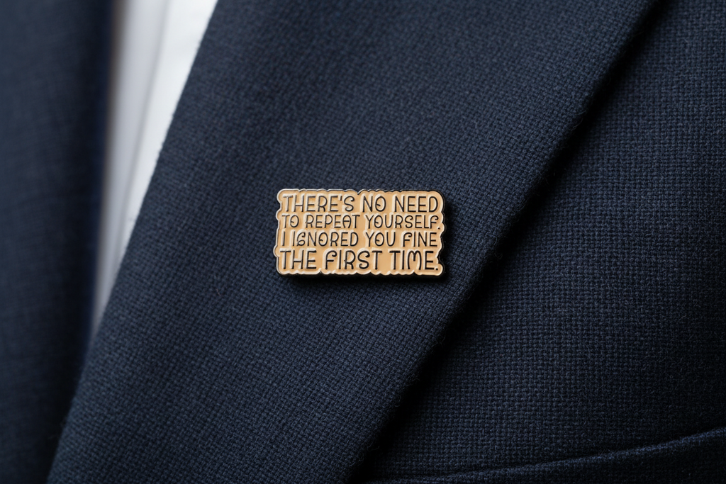 a beige enamel pin with black text on a navy lapel background