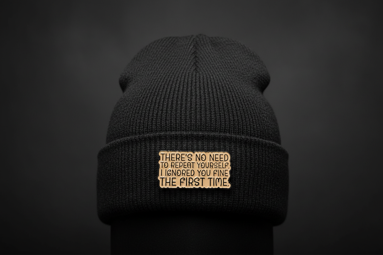 a beige enamel pin with black text on a black beanie background