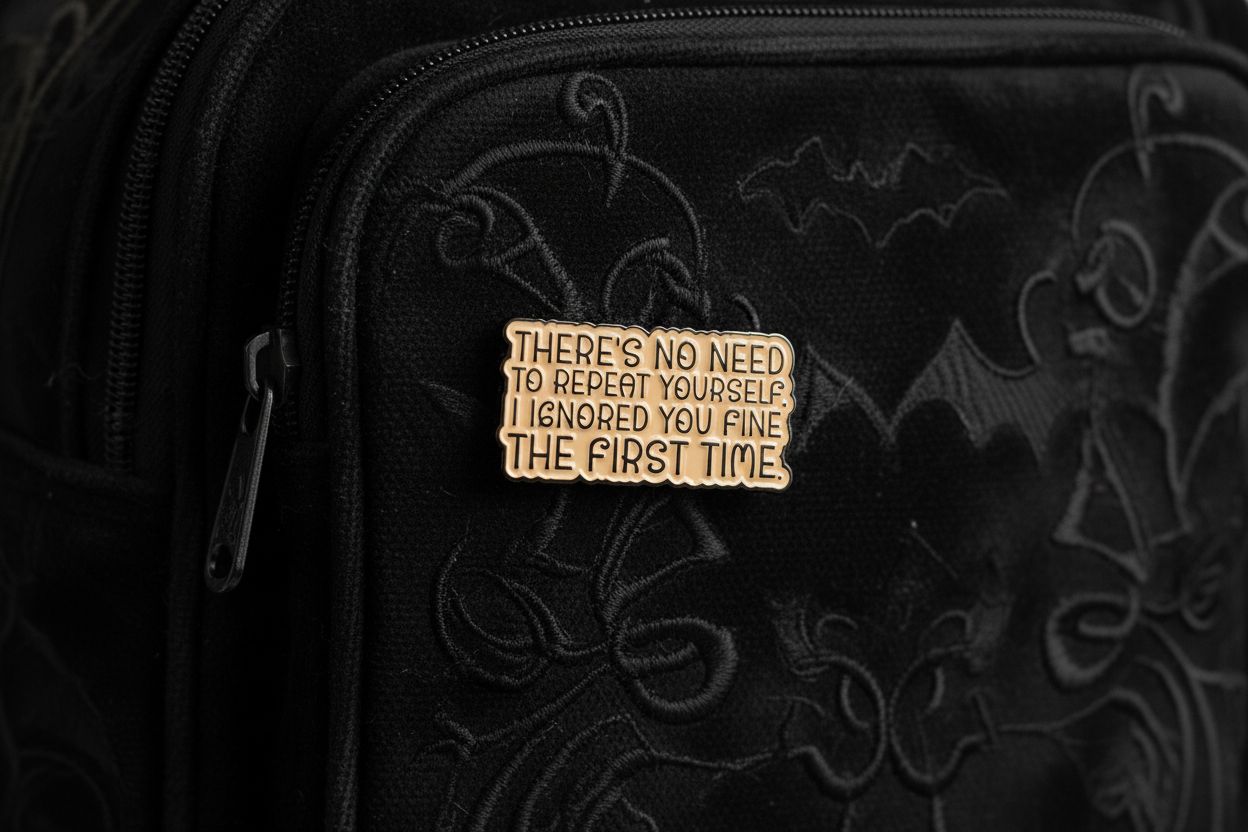 a beige enamel pin with black text on a black bookbag background