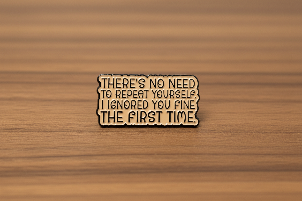 a beige enamel pin with black text on a wood background