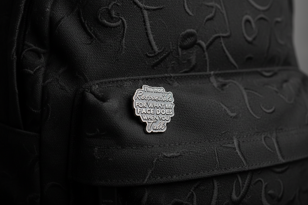 Black enamel pin with text on a black fabric background