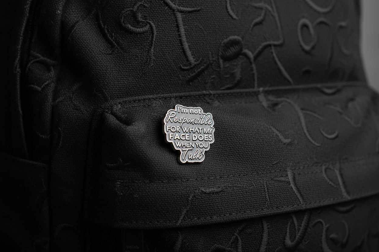 Black enamel pin with text on a black fabric background