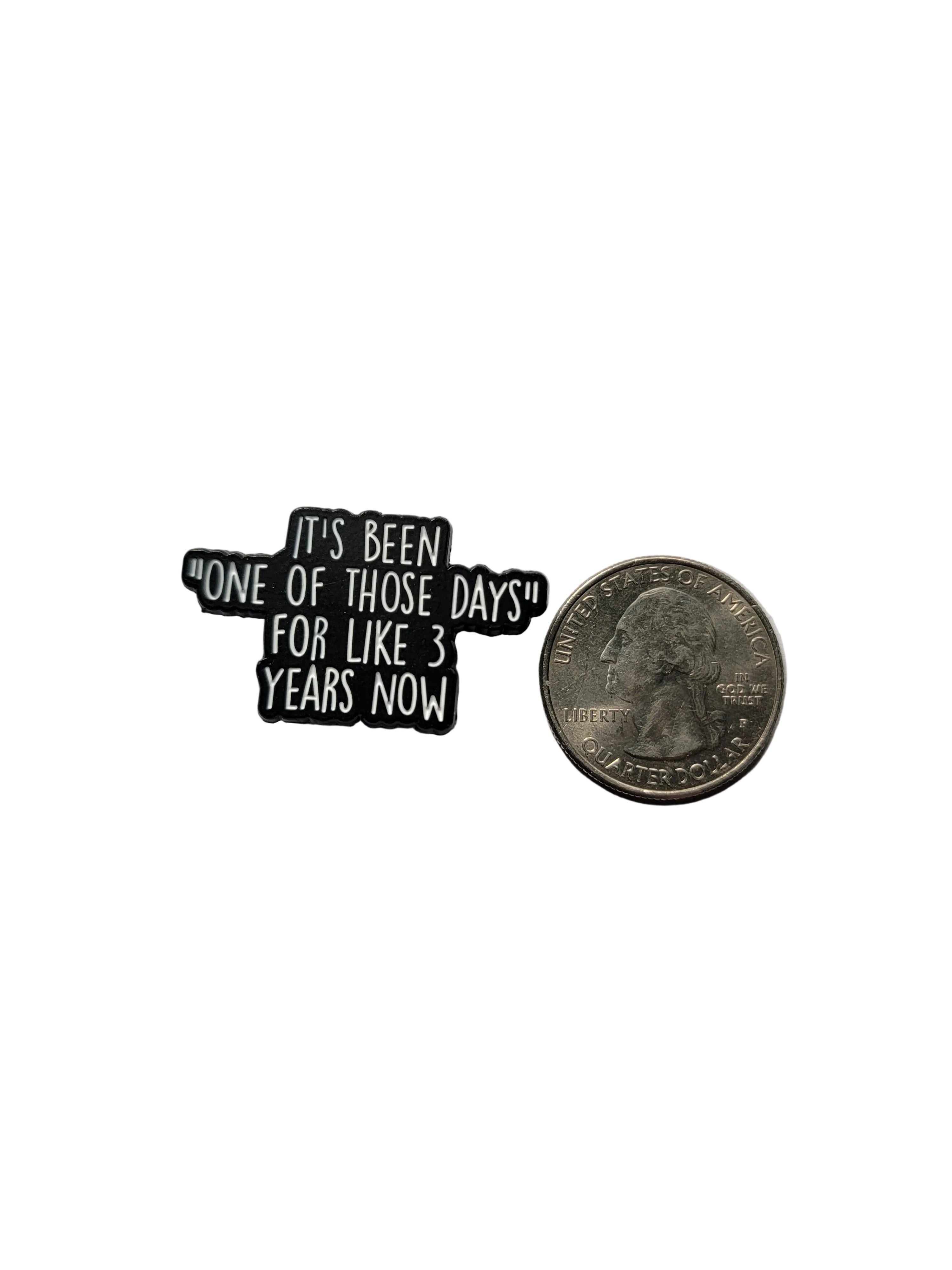 Small black and white enamel pin with text on a gray background