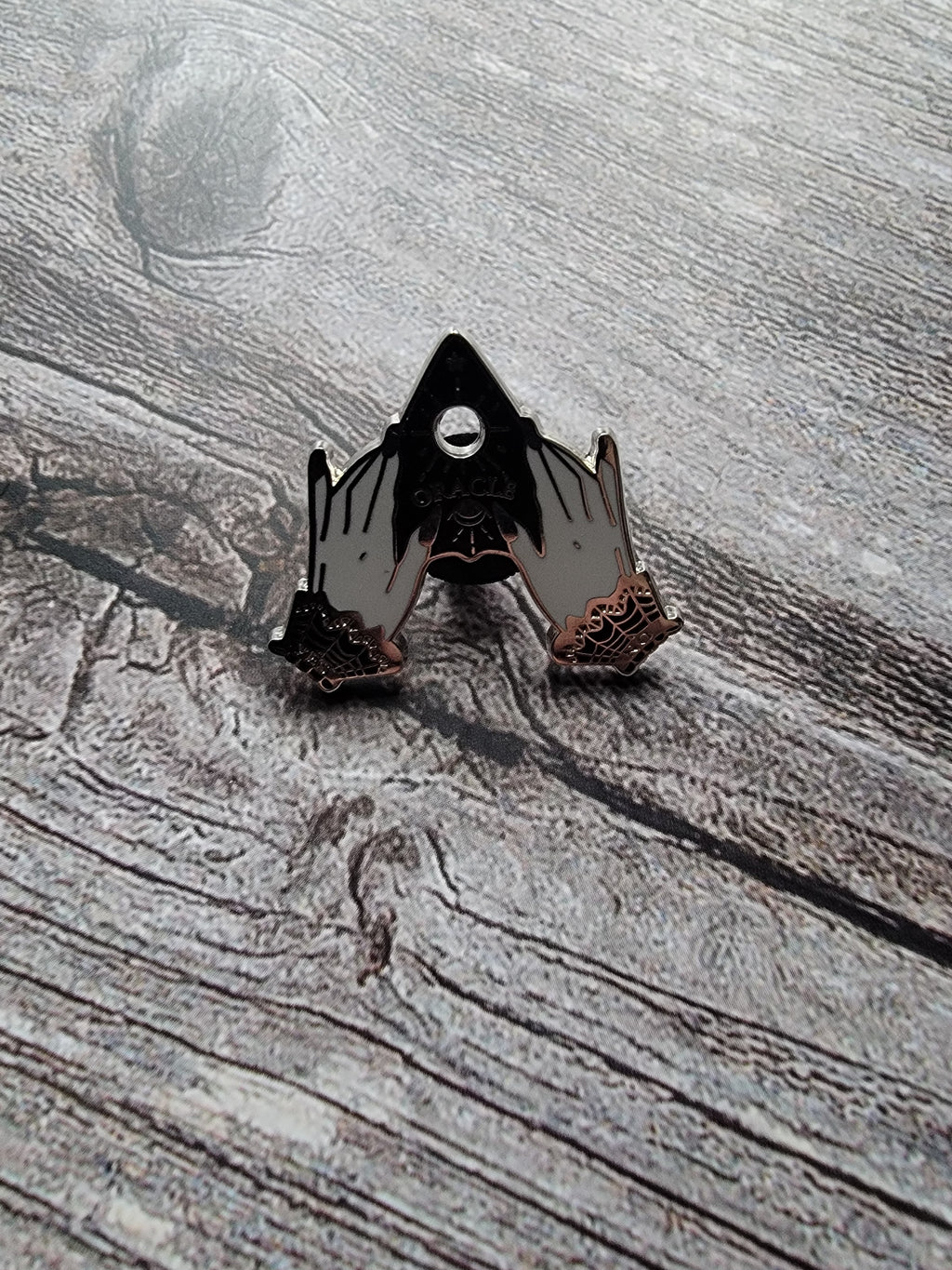 planchette enamel pin on wood background gothic enamel pin with hands holding a planchette 