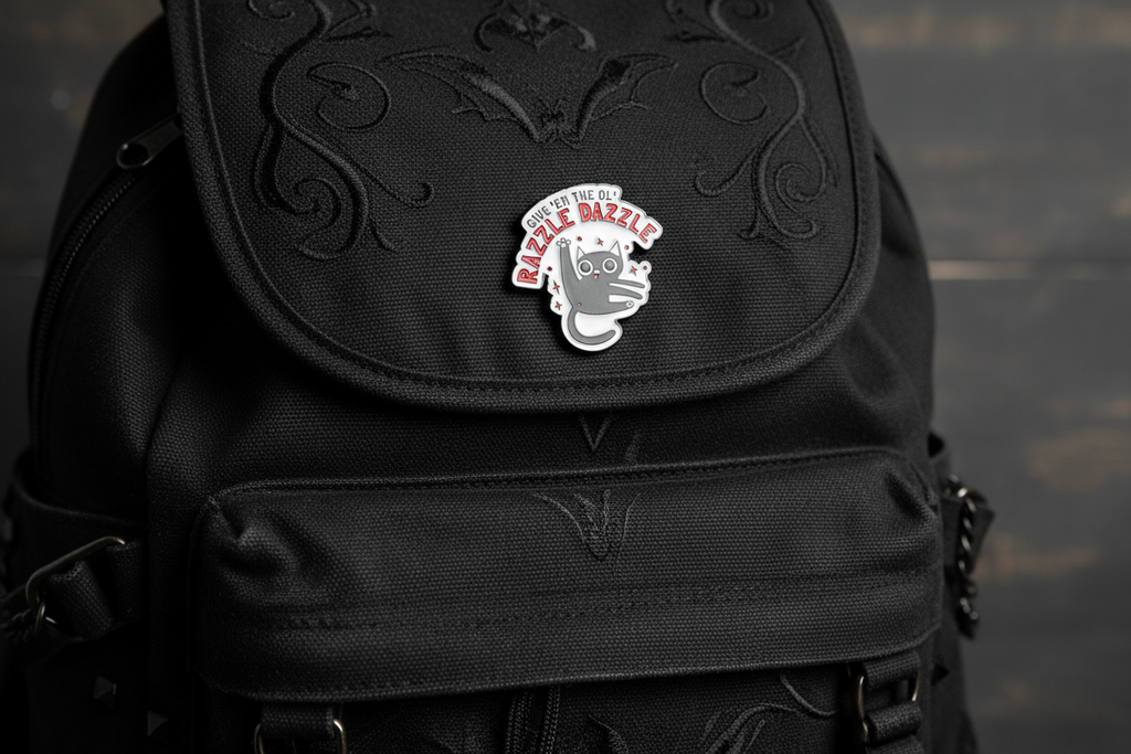 a white enamel pin with a cat and funny saying on a black bookbag background