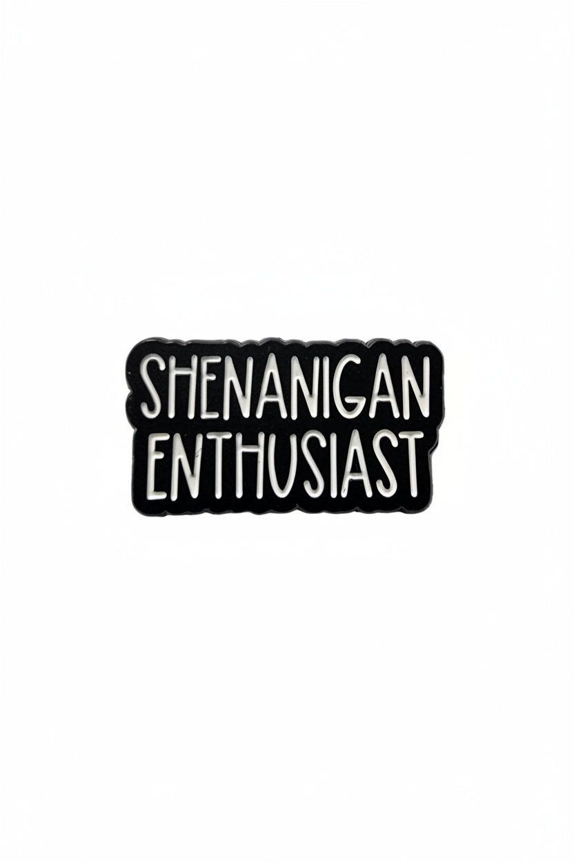 Black and white enamel pin with 'SHENANIGAN ENTHUSIAST' text on a gray background