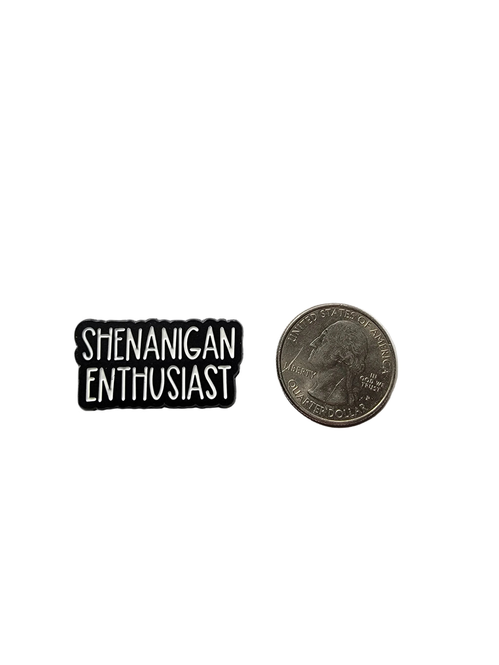 Small rectangular black and white enamel pin labeled 'SHENANIGAN ENTHUSIAST' next to a coin on a light gray background