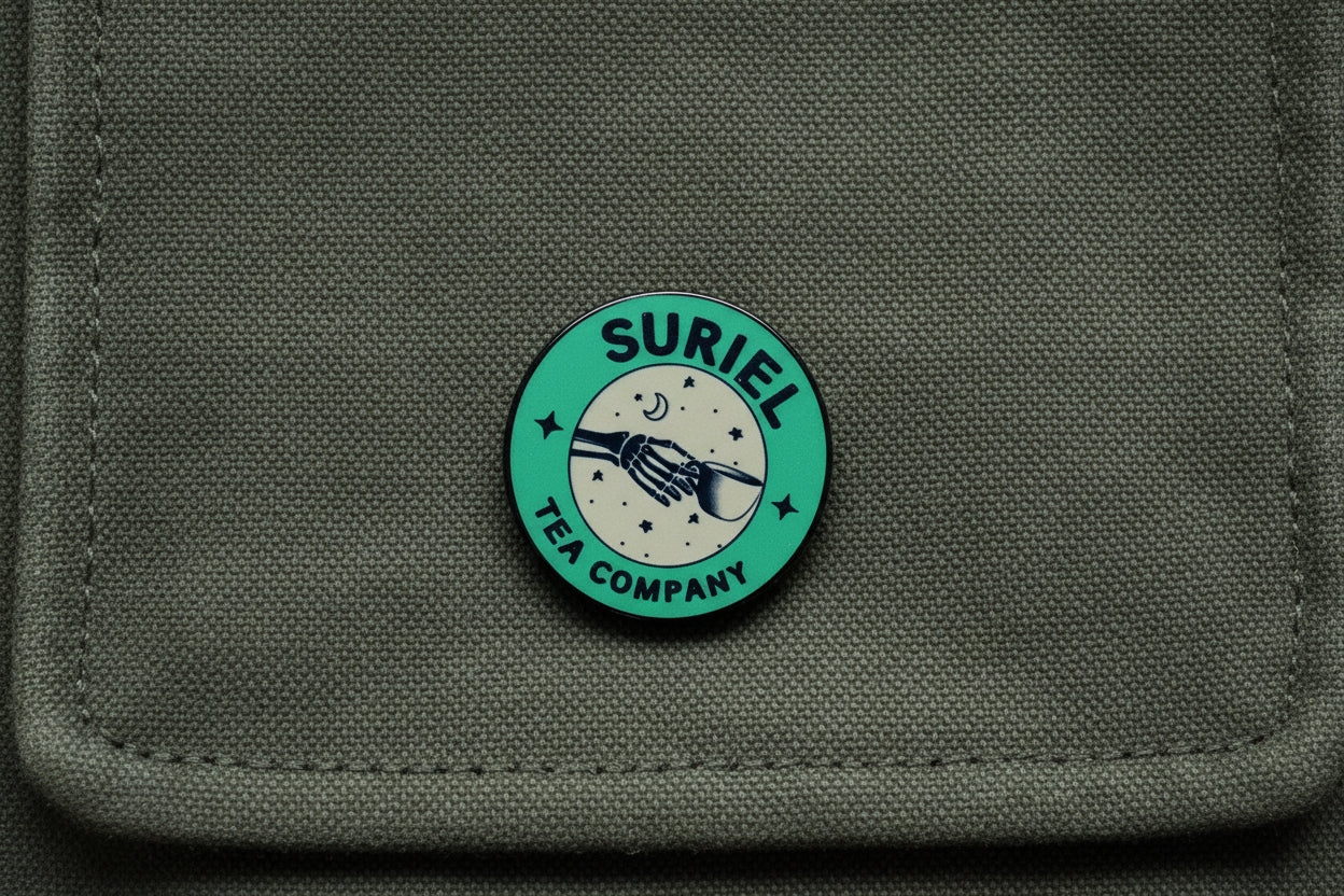 Green round pin with 'Suriel Tea Company' text on a wooden surface