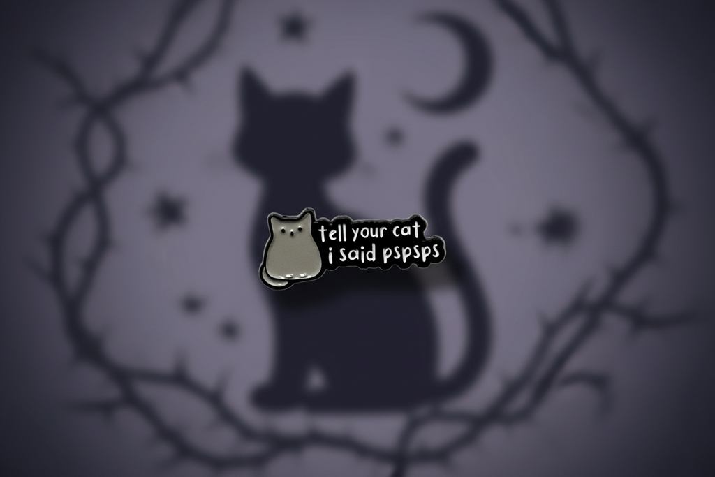 a black enamel pin with white text and a cat on a cat background