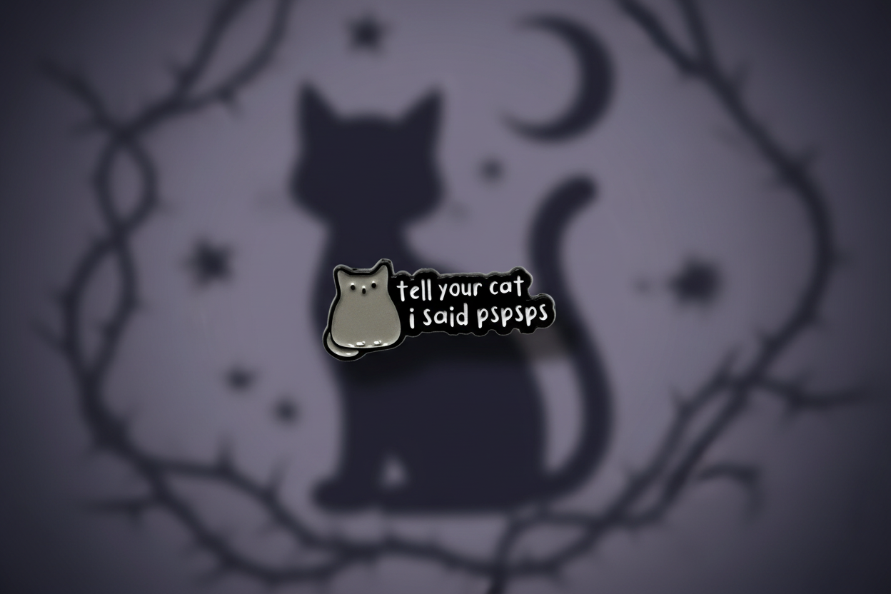 a black enamel pin with white text and a cat on a cat background