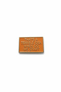 a rectangular orange pin with gold text on a white background