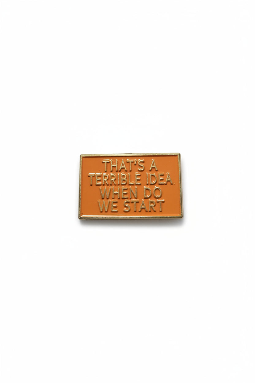 a rectangular orange pin with gold text on a white background