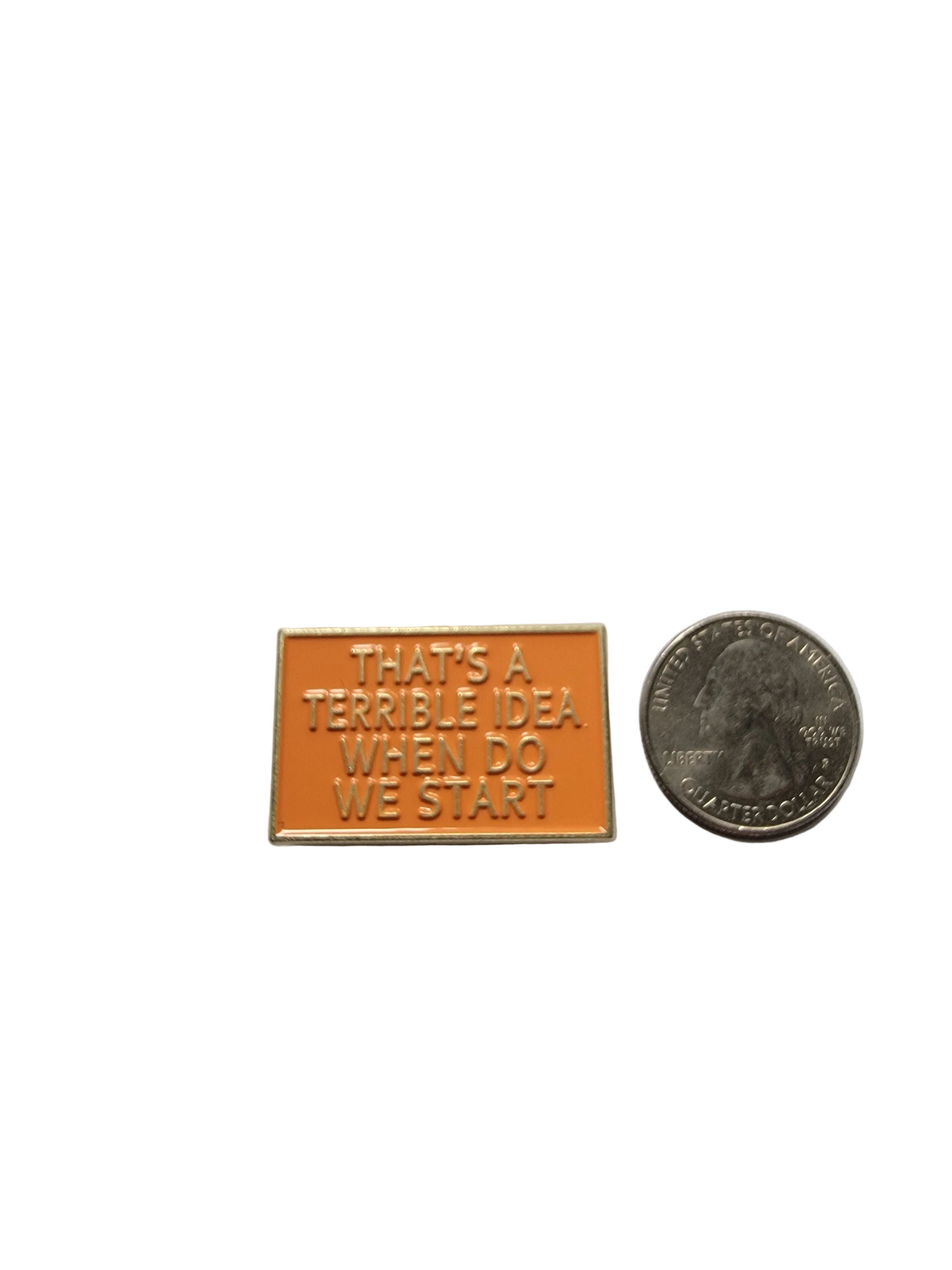a rectangular orange pin with gold text next to a quarter for scale on a white background