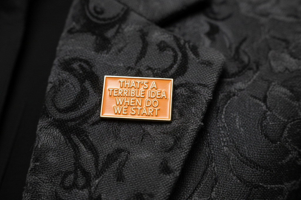 a rectangular orange pin with gold text on a lapel background