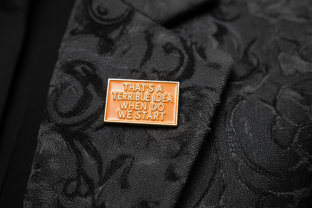 a rectangular orange pin with gold text on a lapel background