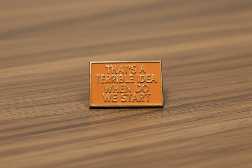 a rectangular orange pin with gold text on a wood background