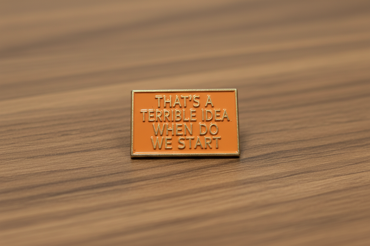 a rectangular orange pin with gold text on a wood background