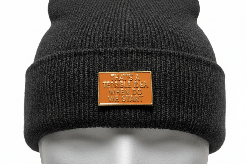 a rectangular orange pin with gold text on a black beanie background