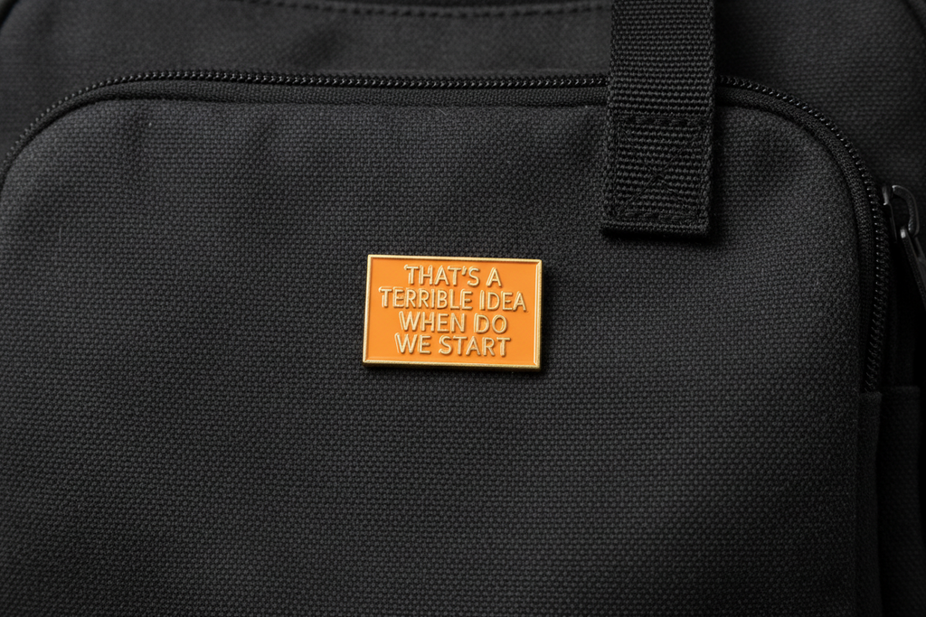 a rectangular orange pin with gold text on a black fabric background
