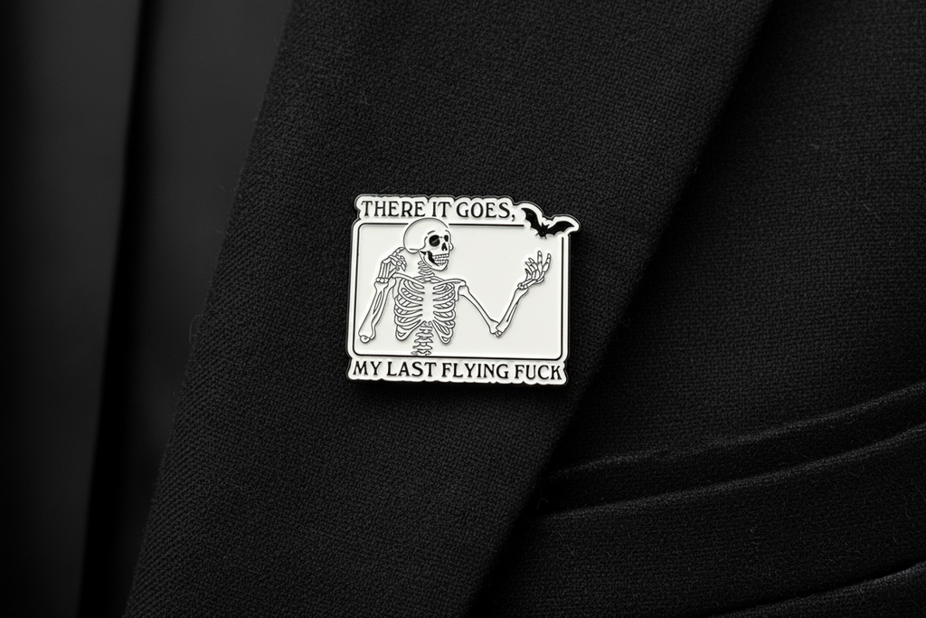 White enamel pin with skeleton and black text on a black lapel background. 