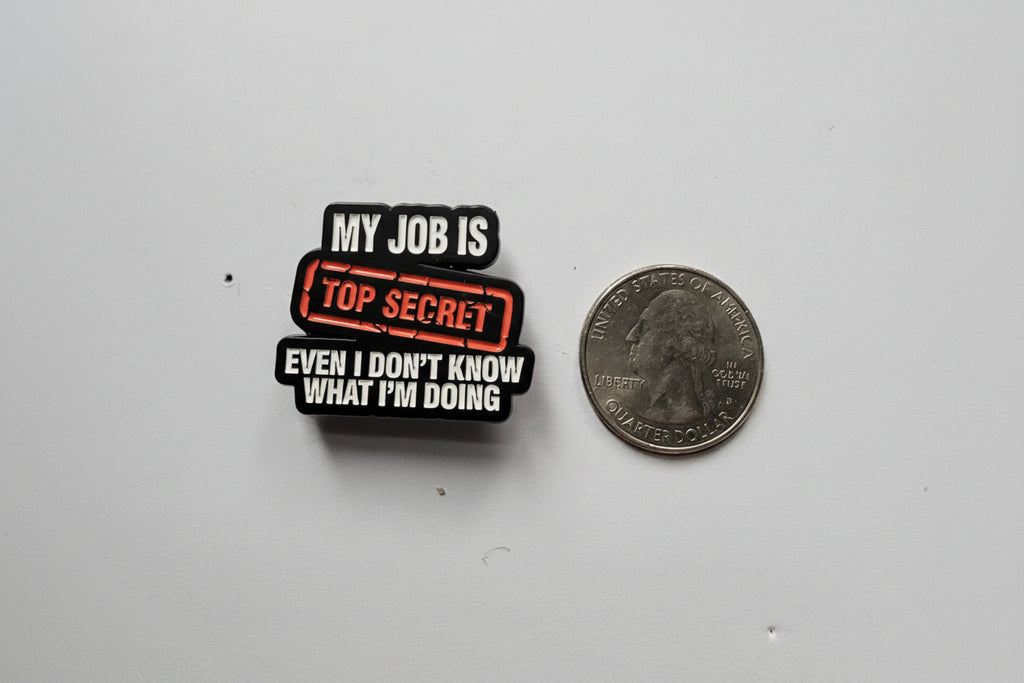Small pin with text on a quarter for scale, on a gray background