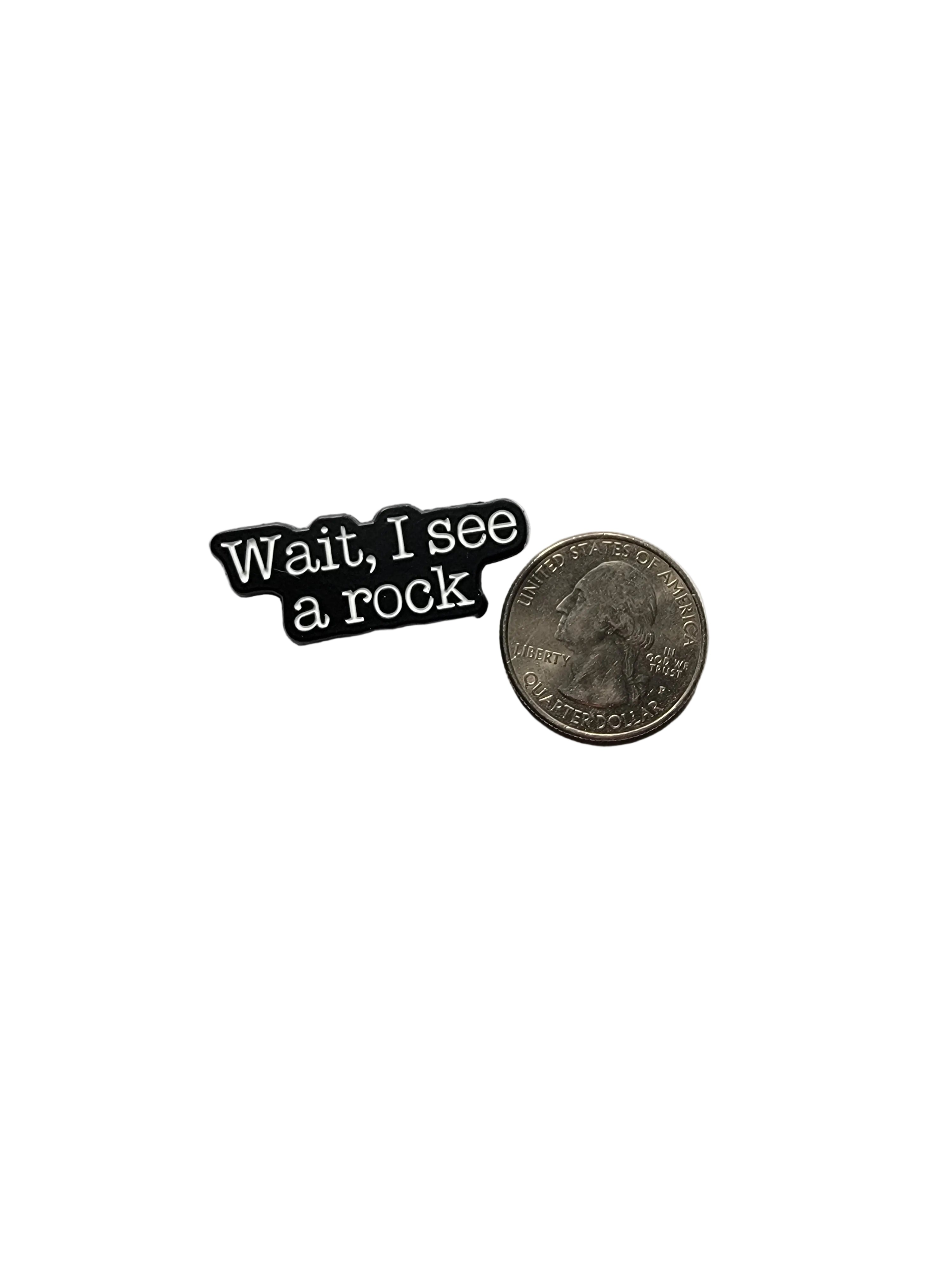 Small black and white pin with text next to a quarter on a white background