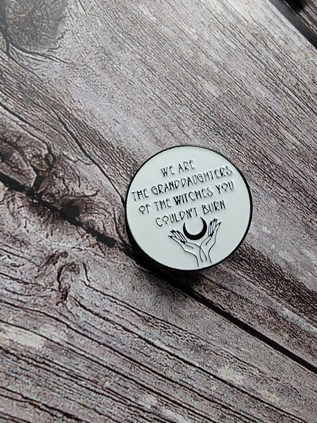 we are the granddaughters of the witches you couldn't burn enamel pin  on wood background spooky enamel pin with moon detail