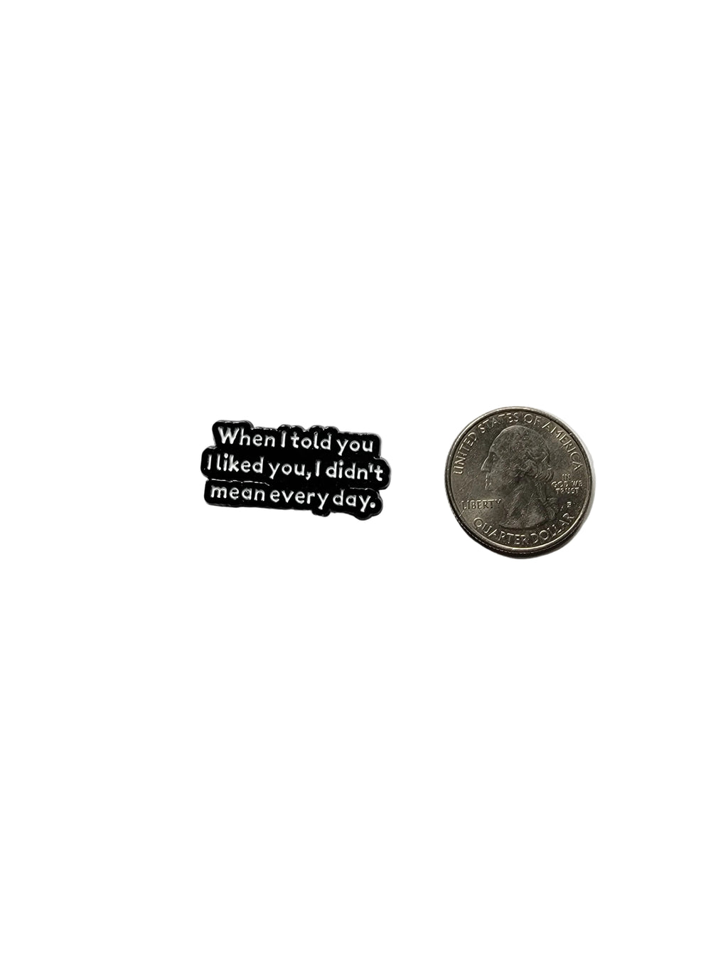 a black enamel pin with white text and a sarcastic saying next to a quarter for size on a white background