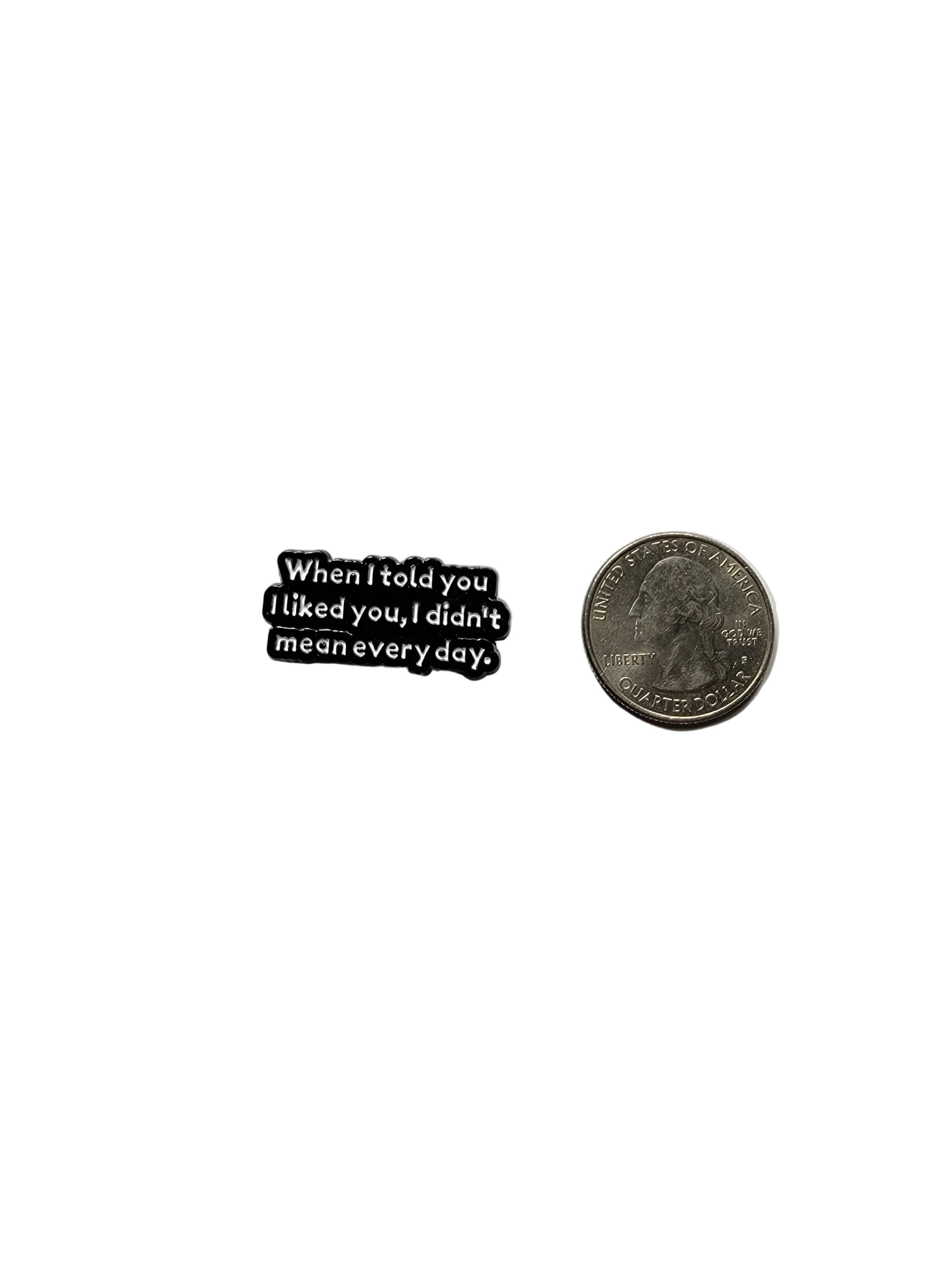 a black enamel pin with white text and a sarcastic saying next to a quarter for size on a white background